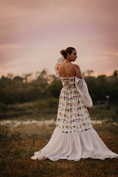 woman stands alone in a dress in a field during an empowerment photo session in rural Saskatchewan. 