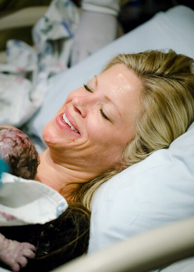 A mother has a relieved smile as she snuggles her new baby after birth. Phot by Diane Owen.