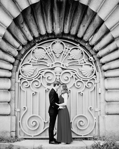A young couple embraces in front of an ornate gate in Paris