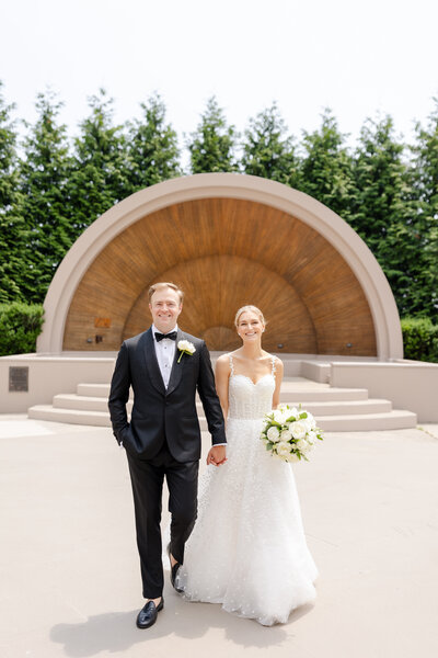 New York Country Club Wedding, Bride and groom holding hands in front of the bandshell at Westchester Country Club