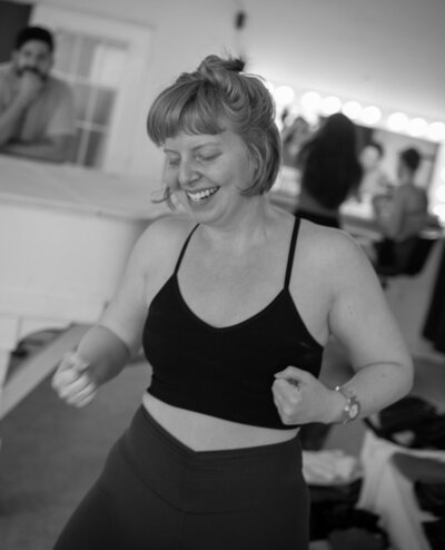 Black and white photo of woman of yoga teacher with short hair and bangs smiling with eyes closed in yoga outfit.