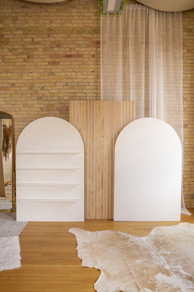 Three wooden backdrops set up side by side. One white with shelves, one wooden slat wall, and one plain white.