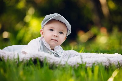 A serene baby lying on a colorful blanket, surrounded by lush green grass in a sunny outdoor setting.