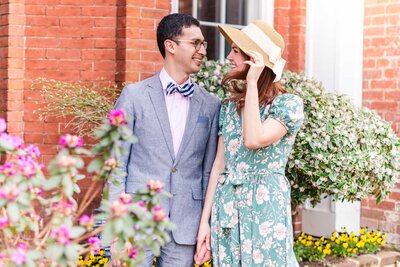 An engaged couple smiles at one another as the wind blows her hair during their engagement session in Old Town Alexandria