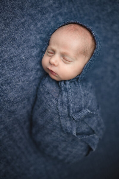 newborn wrapped in blue blanket laying on a blue blanket
