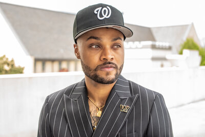 a man in a black fitted hat wearing a black and white striped suit with a small "w" pin looking to the right of the camera. photographed by Millz Photography in Greenville, SC