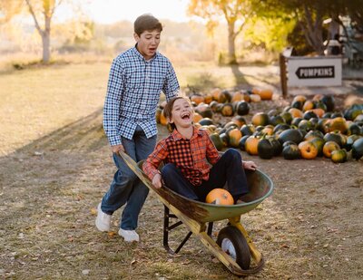 Big brother pushes his little brother in a wheelbarrow during as they are both laughing during their family photo session with Colorado family photographer Avenir Photo Co.