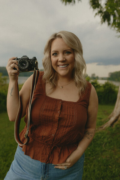 Professional photographer captured in a candid moment, radiating joy while holding her camera in a sun-dappled garden setting