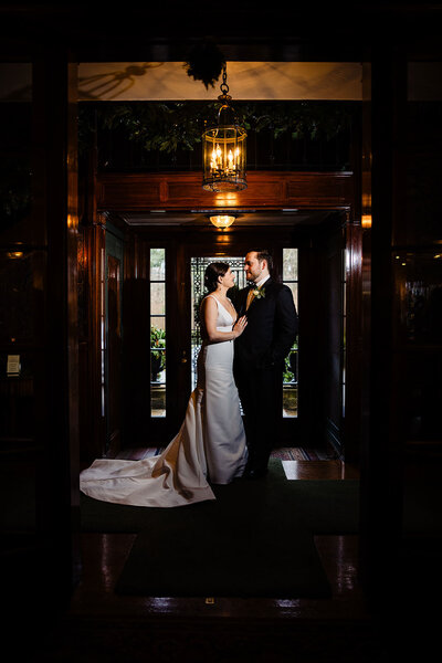 A bride and groom standing in a dark doorway, lit by romantic light at their lord thompson manor wedding