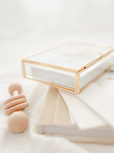 A glass keepsake box filled with fine art photo prints beside a wooden baby rattle — Portrait photography in Raleigh.