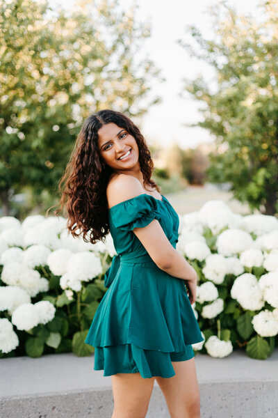 Senior girl in a green dress posing in front of white hydrangea bushes