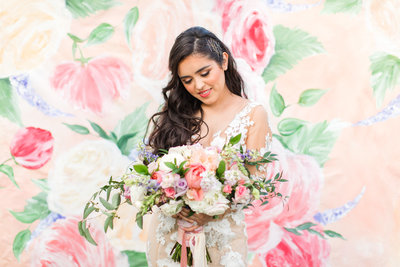Bride with colorful florals in front of painted wedding backdrop painted By Brittany Branson