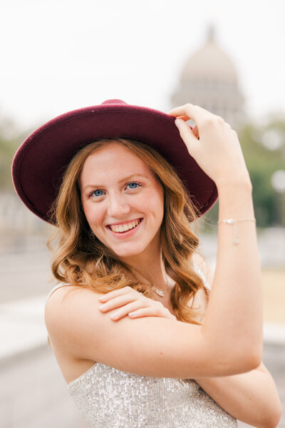 a girl smiling while holding onto the brim of her hat