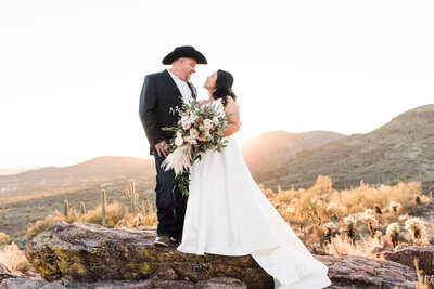 bride and groom standing on rock with sunset behind them
