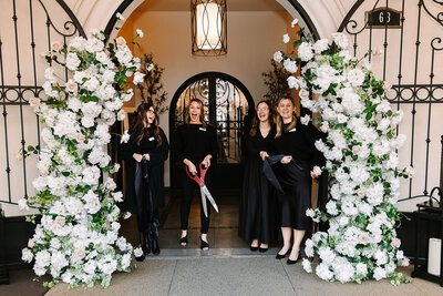 A group walks confidently out of the front entrance of SoHo63, a Chandler wedding and event venue, under its signature white stucco arch and bold signage. The sunny exterior and wrought iron doors highlight the venue’s stylish presence in Downtown Chandler.