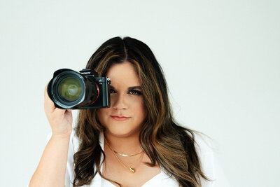 Adriana of Adriana Montoya Photo holding her camera to her face. She has a serious expression.