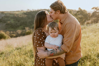 Image of a couple kissing and holding their child