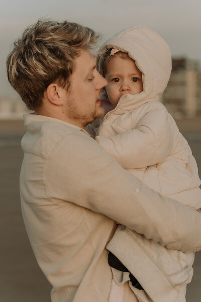 Papa houdt dochter in jas vast op zijn armen tijdens familie fotoshoot op het strand