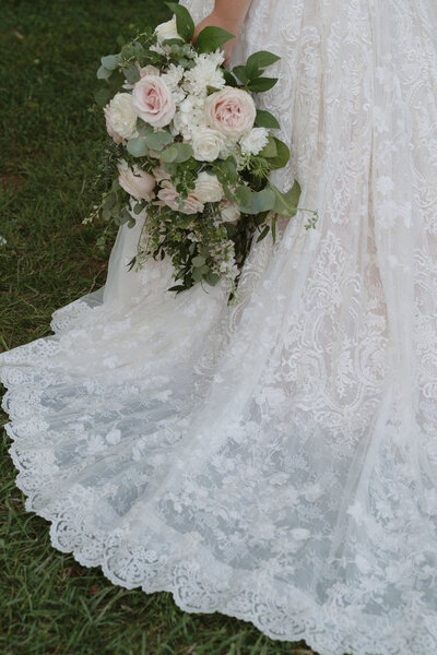 The train of a wedding gown with the bride's bouquet at Hidden Meadows in Northeast, TN