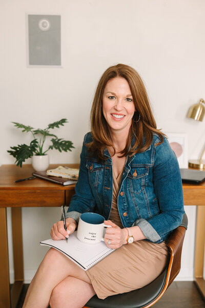 Lindsay sitting in her office taking notes while holding a cup of coffee