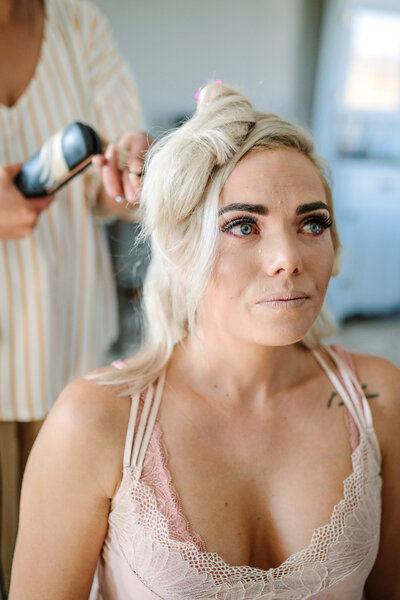 Bride having her hair done, shedding a tear as the reality of her wedding day sets in, captured in a candid, emotional moment.