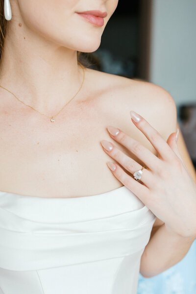 bride touches chest with emerald cut engagement finger hand