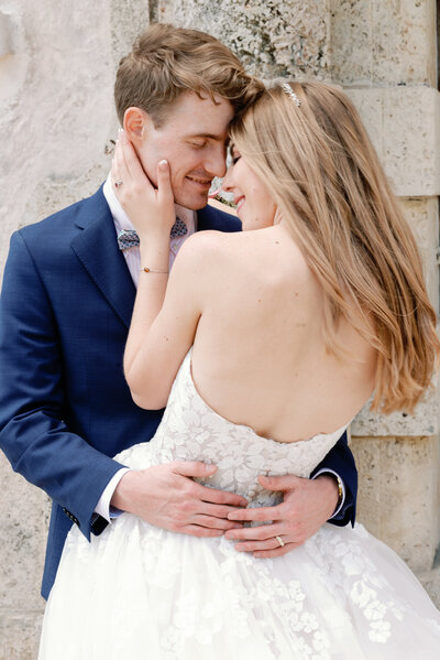 bride and groom wrapped in a romantic embrace. Her back is showing, grooms hands are around her waist. Brides left hand in on his neck and jawline and their foreheads are touching