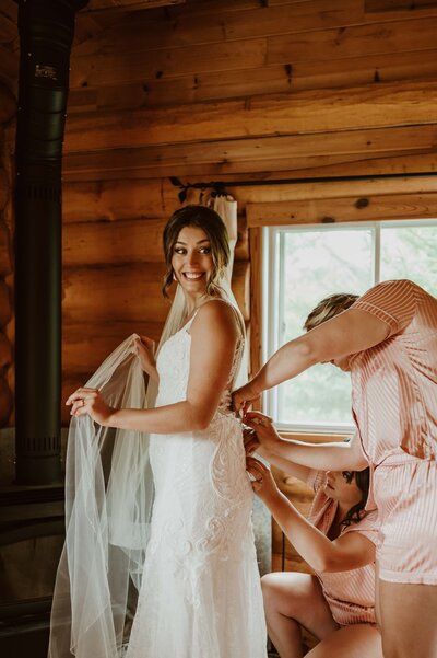 Bride waits in excitement  for her first look and her bridesmaids do up her dress