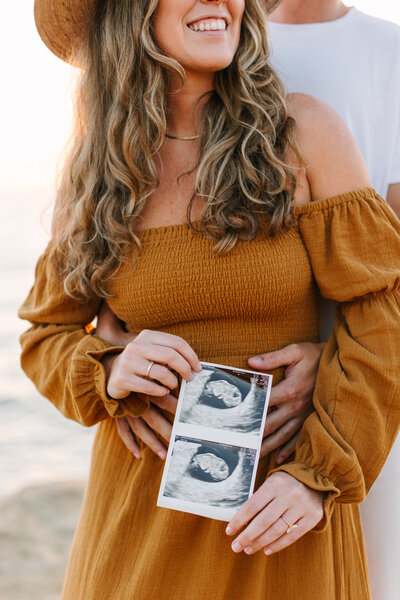 maternity and pregnancy announcement photo of mom holding sonogram and dads arms wrapped around mom