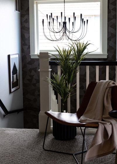 A stairway landing featuring a modern chair with a throw blanket across the back, a hanging light fixture and a house plant.