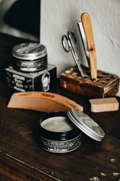 A collection of grooming tools and products, including scissors, a comb, and styling pomade, neatly arranged on a wooden surface, showcasing the high-quality equipment used at 212 Salon, Spa, & Barbershop.