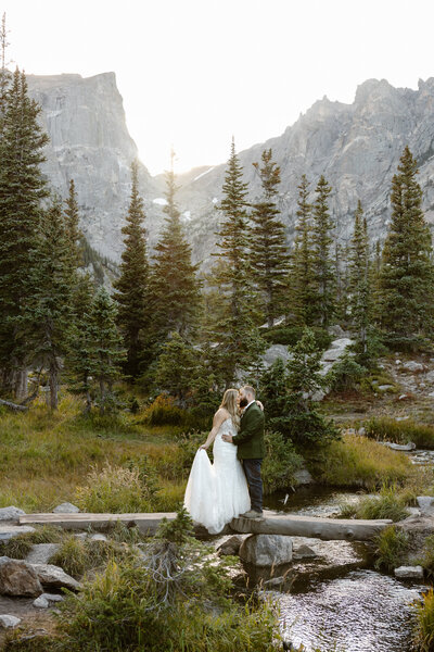 groom helping bride climb over rocks on their colorado hiking elopement