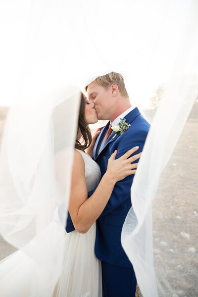A bride and groom share a passionate kiss under a veil captured by an Austin-based wedding photographer.