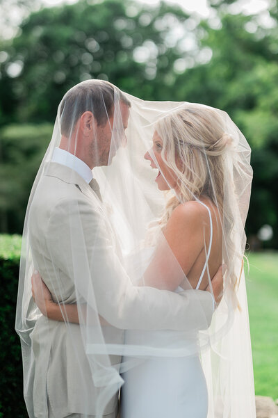 A bride and groom sharing a moment tucked under the bride's veil together