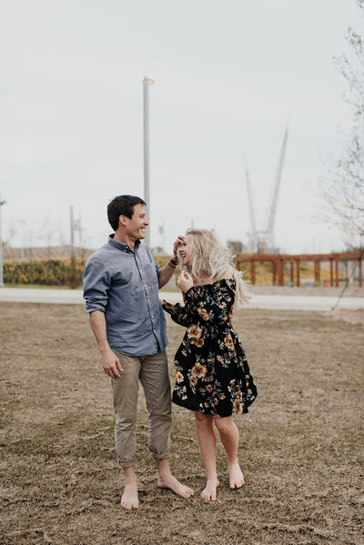 Couple laughing together outside barefoot during their engagement session