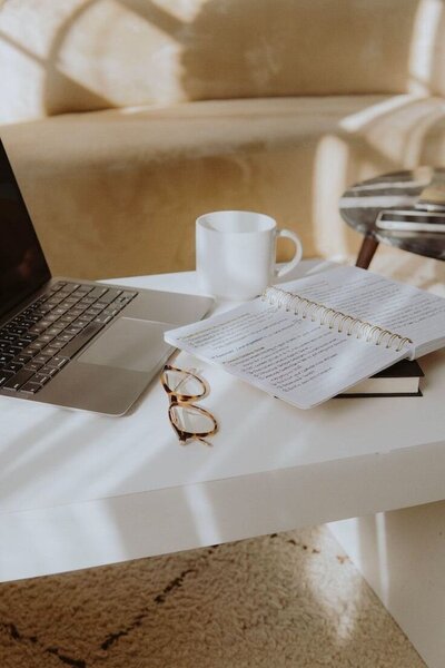 Espace de travail avec un ordinateur, des lunettes, une tasse de café et des notes sur un cahier.