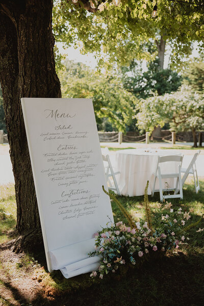Large  white  menu sign with grey handlettering  on a large board for Stone Acres Farm wedding in Stonington, Connecticut.
