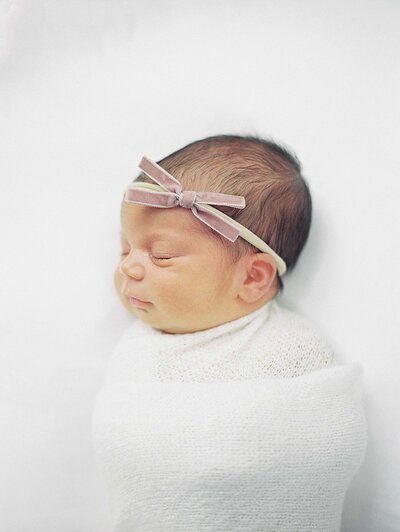 photo of a newborn baby girl with a pink bow sleeping on a white blanket by richmond va family photographer Jacqueline Aimee Portrait