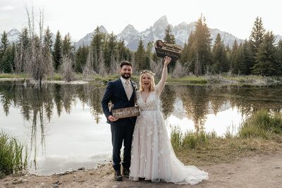 A couple holds up a national park sign and celebrates after their elopement in Grand Teton National Park.