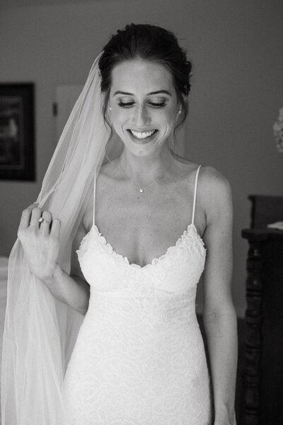Black and white photo of bride smiling and looking down while holding her veil