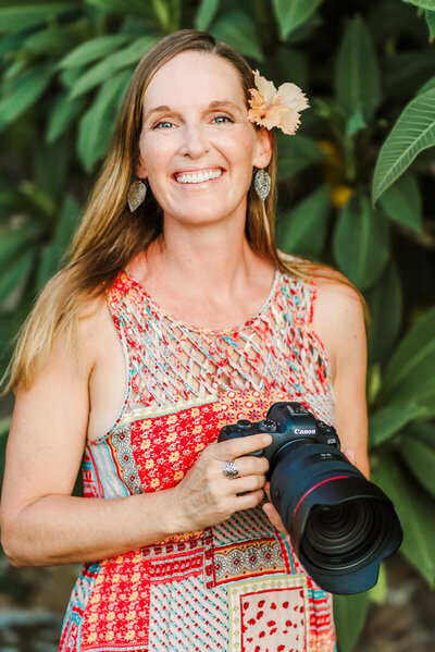 Laura Pittman Photographer, holding camera and smiling with a flower behind her ear