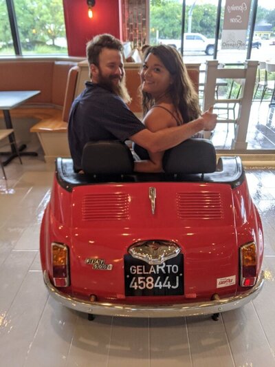 Ms. Mia and her husband sitting in a fun, little red car