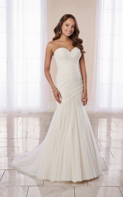 MODERN FIT-AND-FLARE WEDDING DRESS WITH RUCHING A dreamy, sexy silhouette, this Stella York gown takes classic style to the next level. The strapless sweetheart neckline of Style 7075 offers a clean, highlighted decolletage with a full-construction back for maximum support. Soft, sparkling tulle enwraps the figure with delicate ruching for a textured elegance that draws in the waist and enhances the figure. Flaring below the hips are gathered layers of tulle for a mermaid-style effect, following into a lush, frothy train detail. This gown zips beneath fabric-covered buttons, and is also available in plus sizes.