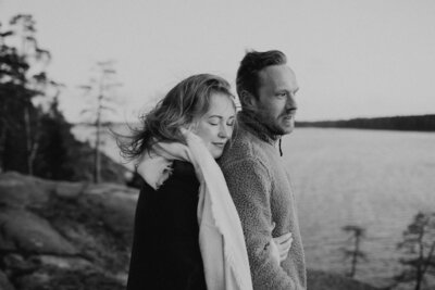 Pari seisoo rantakalliolla nainen halaten miestä selän takaa ja nojaten päätä miehen olkapäähän silmät suljettuina Kivenlahdessa Espoossa