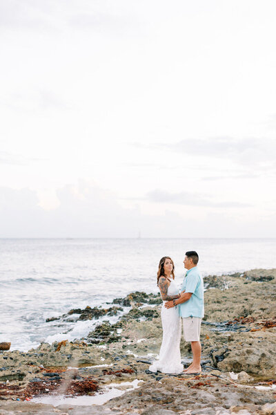 bride and groom stand on rocky beach in Cancun, Mexico