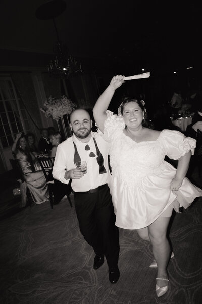 Black and white film photo of two brides holding hands and smiling during their Boston wedding — captured by a film wedding photographer at Castillo Holliday Photo + Film