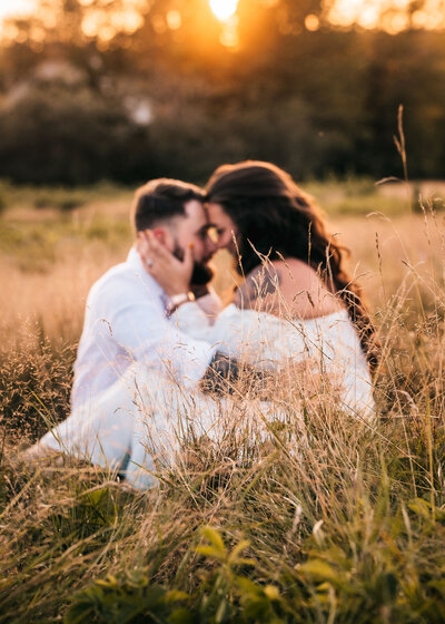 Engaged couple sitting and cuddling in field at sunset at Wagon Hill in Durham NH by Lisa Smith Photography