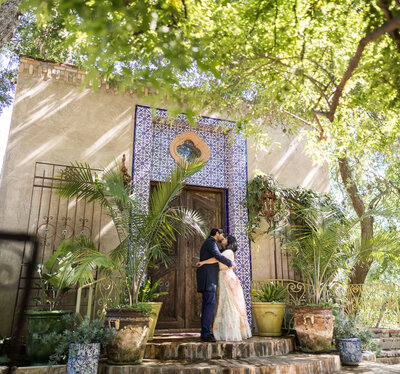 Couple kissing in front of blue-tiled doorway surrounded by greenery