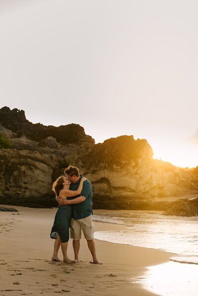 A couple embracing each other on the beach, kissing with the sunset in the background.