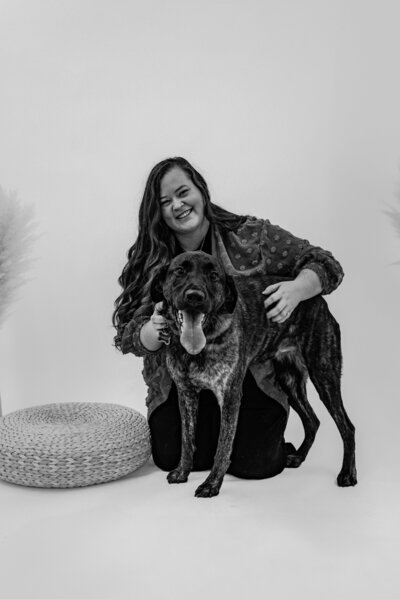 Large brindle-colored dog sitting beside a woven floor pillow, being lovingly embraced in a cozy, light-filled studio setting—captured in a warm and intimate pet photography session in Portland